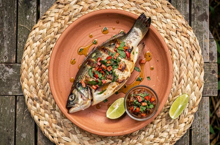 Poisson grillé nappé de sauce chien servie sur une assiette en terre cuite avec citron vert en Guadeloupe